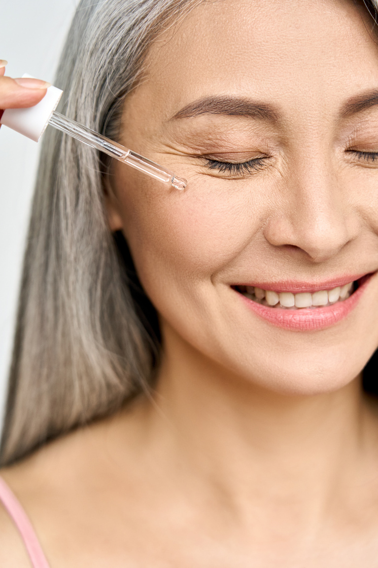 Smiling Senior Woman Applying Cosmetic Serum on Face