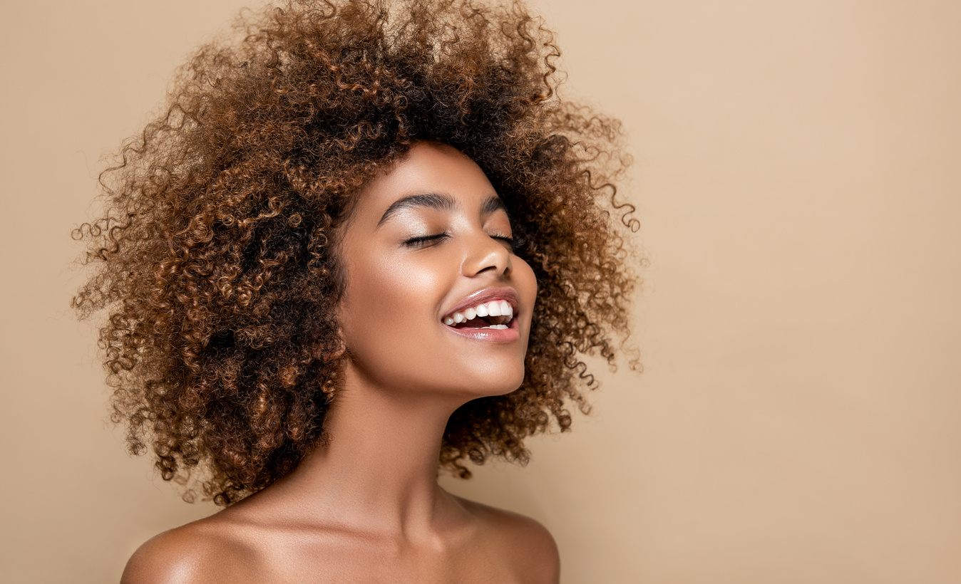 Natural Afro hair. Wide toothy smile and expression of gladness on the face of young brown skinned woman. Afro beauty.